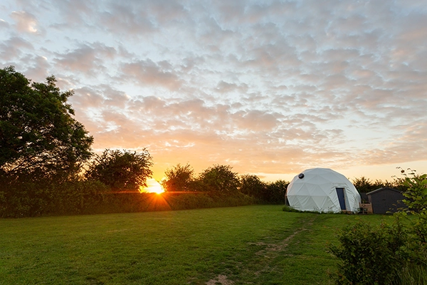 A grass campsite with a dome from TruDomes. The sun is setting in the background