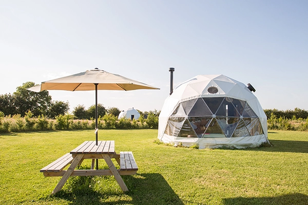 A grass campsite with a table and a dome from TruDomes